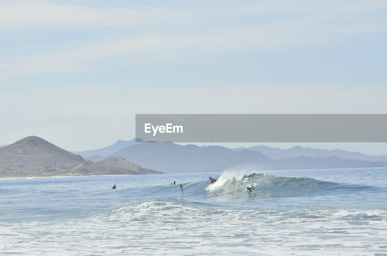 Surfers ride a wave in the pacific ocean off the coast of baja california sur, pescadero, mexico