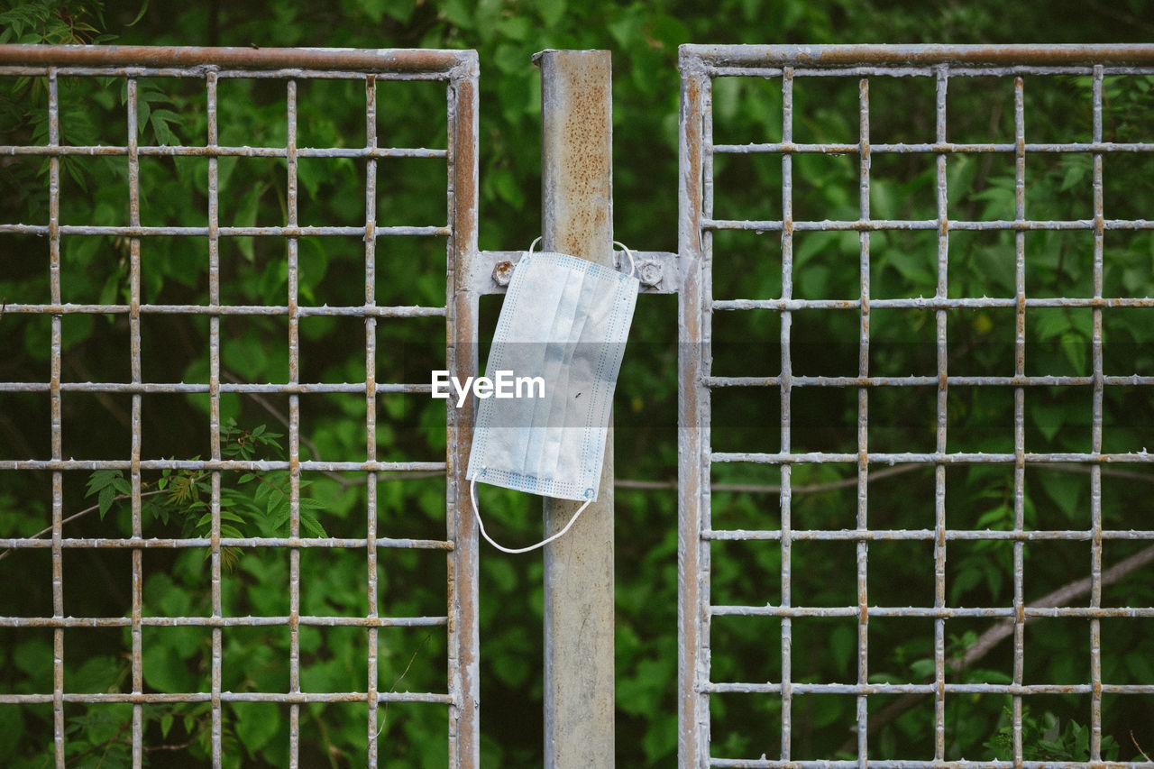 CLOSE-UP OF WOODEN POST HANGING ON FENCE AGAINST PLANTS