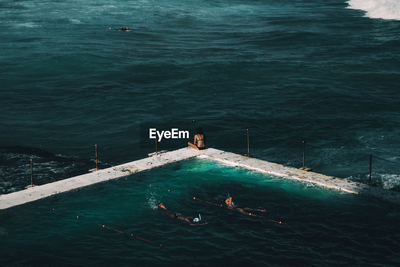 People in swimming pool against calm blue sea