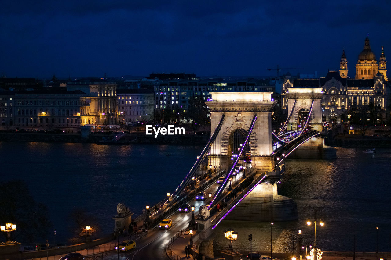 ILLUMINATED BRIDGE OVER RIVER AT NIGHT