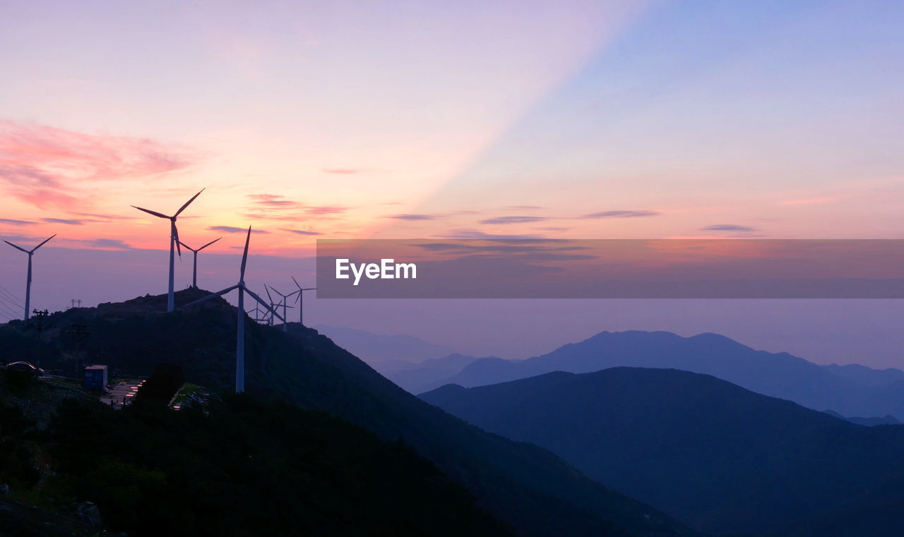 Windmills on mountain against sky during sunset