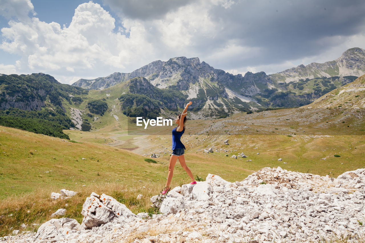 Side view of woman standing on rocks against landscape