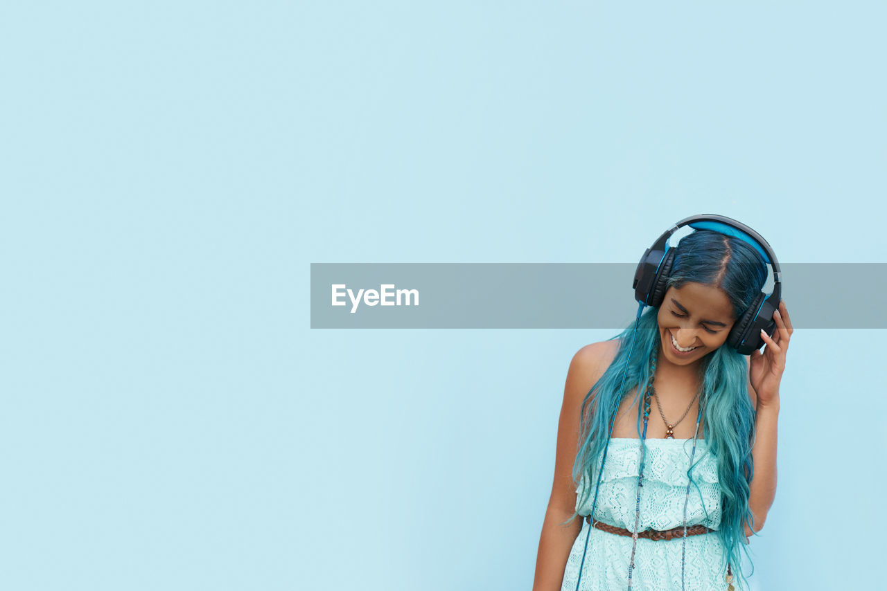 Young woman listening music against blue background