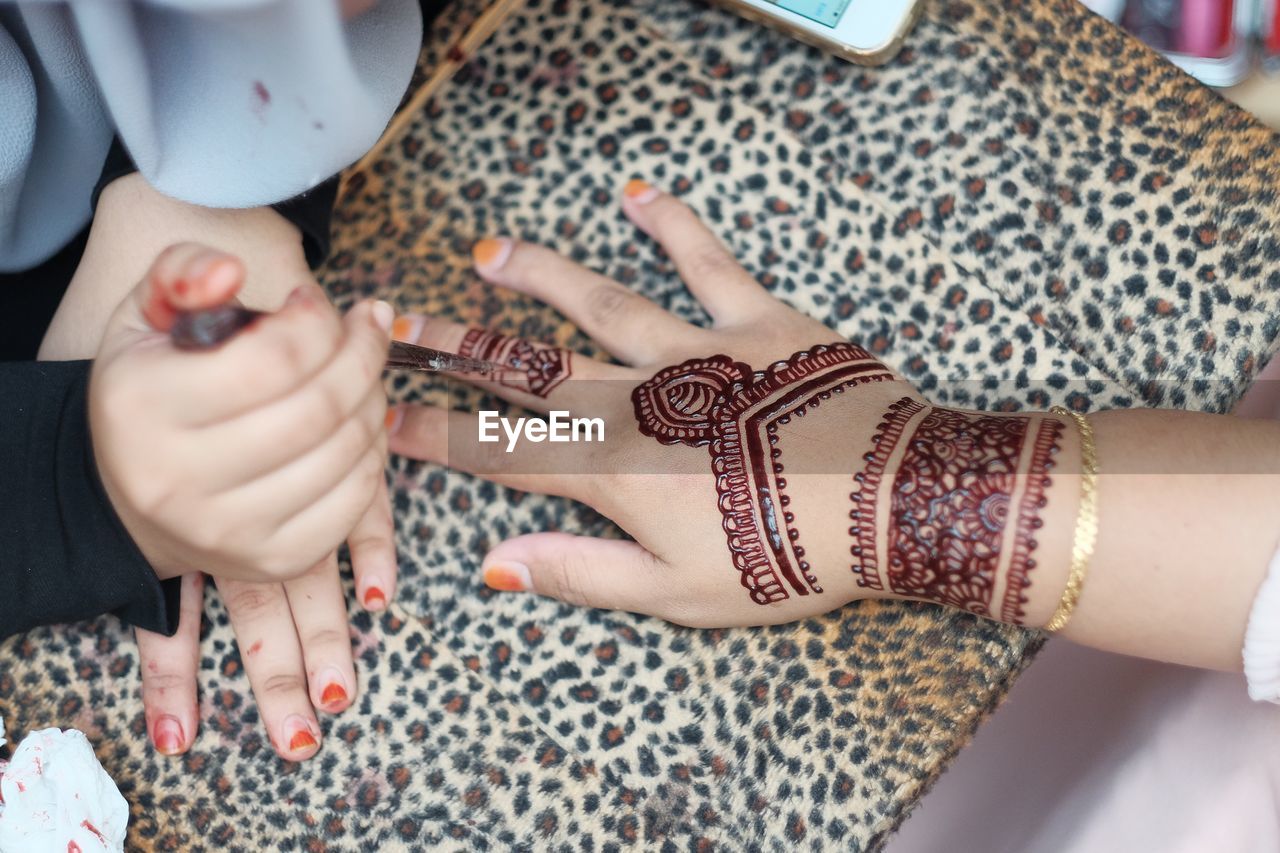 Cropped image of beautician applying henna tattoo on woman hand