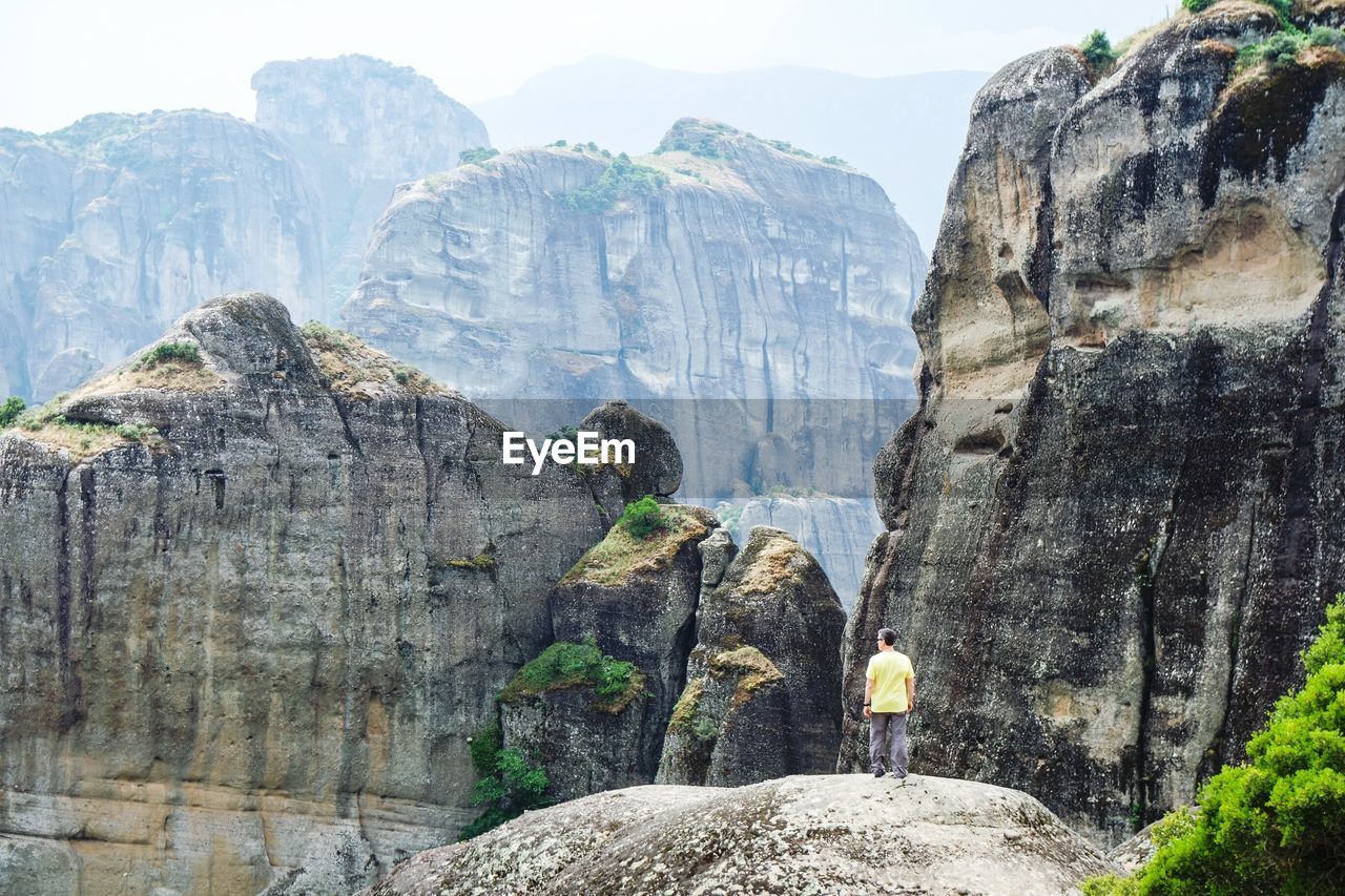 Rear view of man standing on rock against mountains