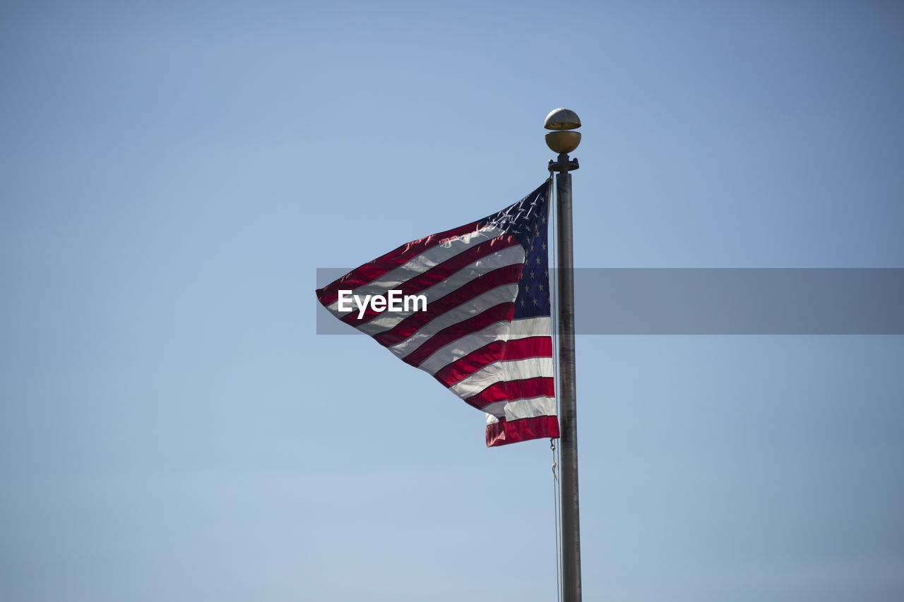 American flag waving vigorously in the wind against a blue sky