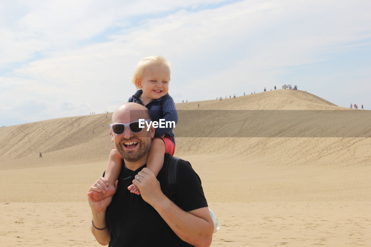 PORTRAIT OF SMILING BOY ON BEACH AGAINST SKY