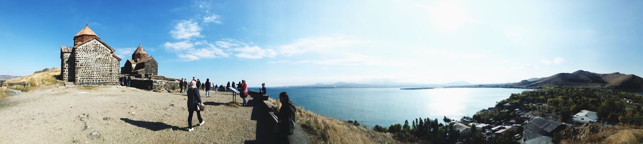 Panoramic view of people visiting temple by lake against sky during sunny day