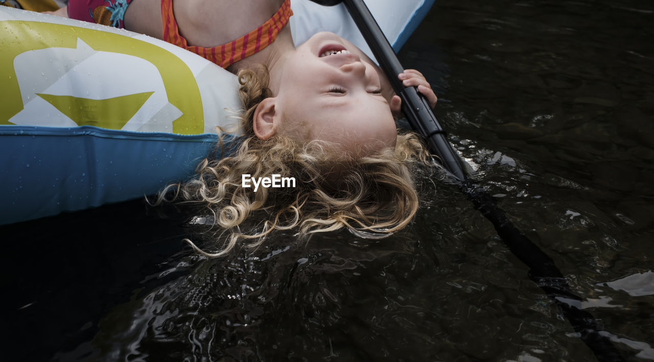 High angle view of happy cute girl lying in inflatable raft on lake