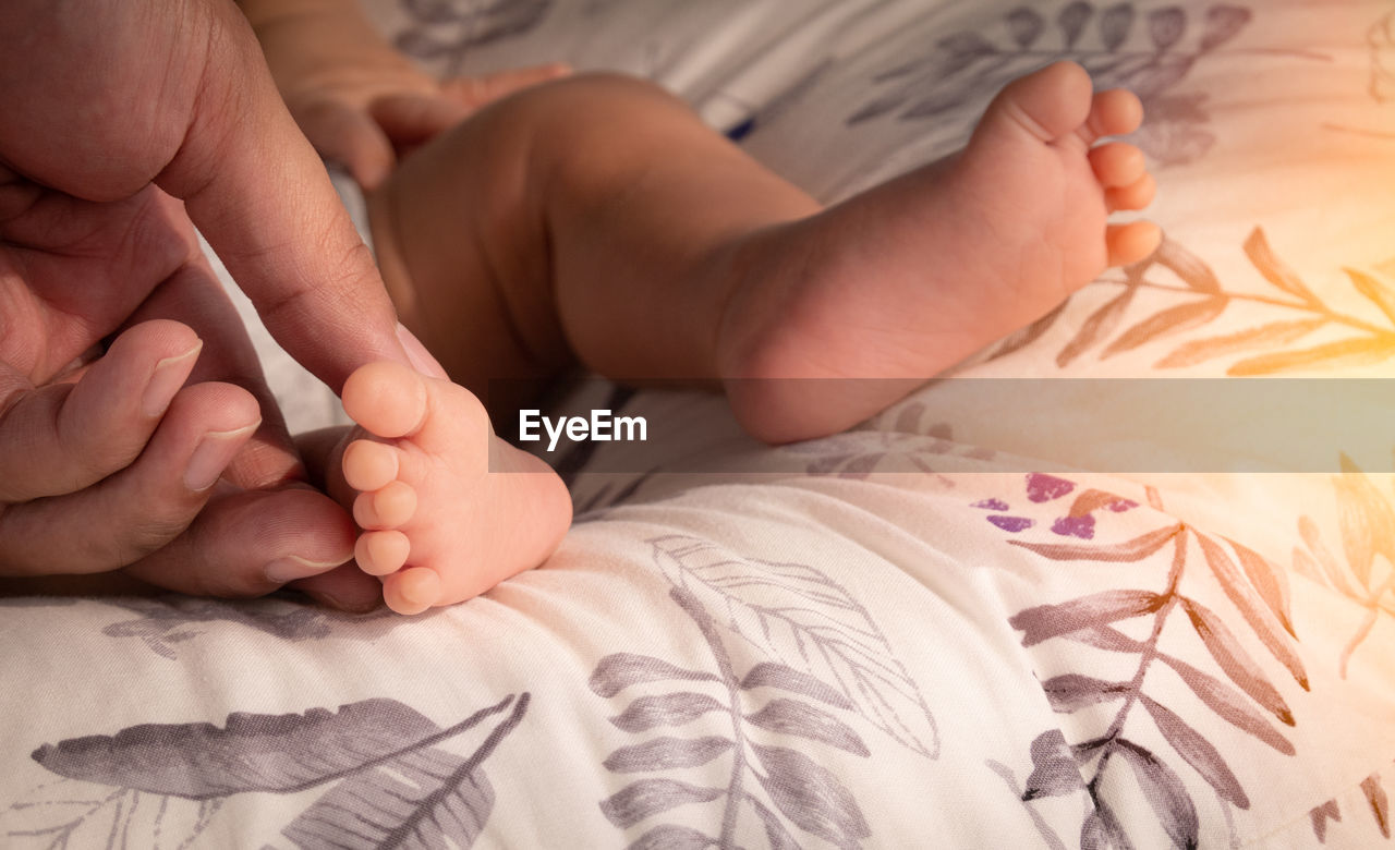 Low section of baby lying on bed