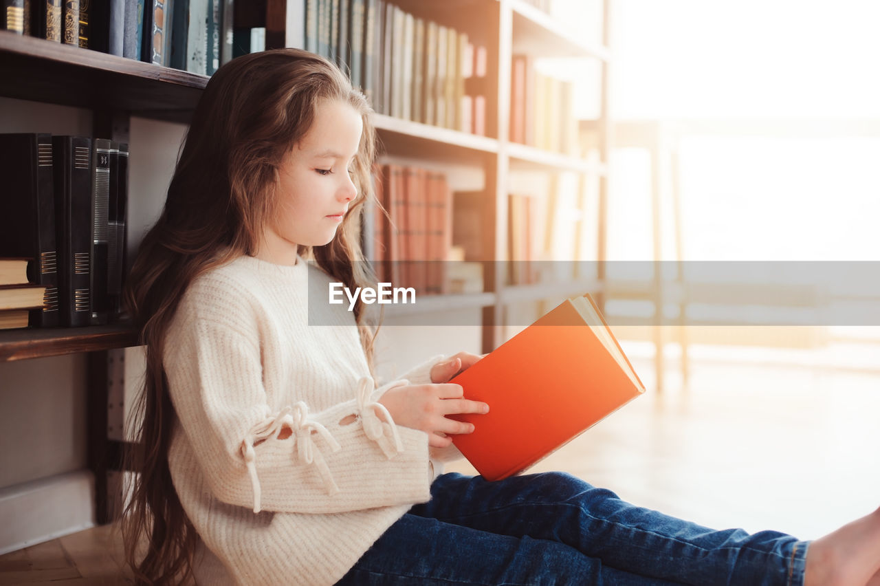 Cute girl opening book while sitting at home