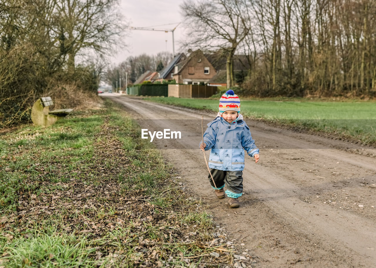 Full length portrait of girl walking on dirt road against bare trees