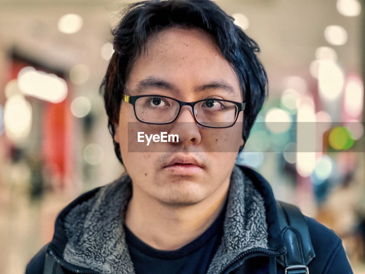 Portrait of young asian man in eyeglasses against illumination.