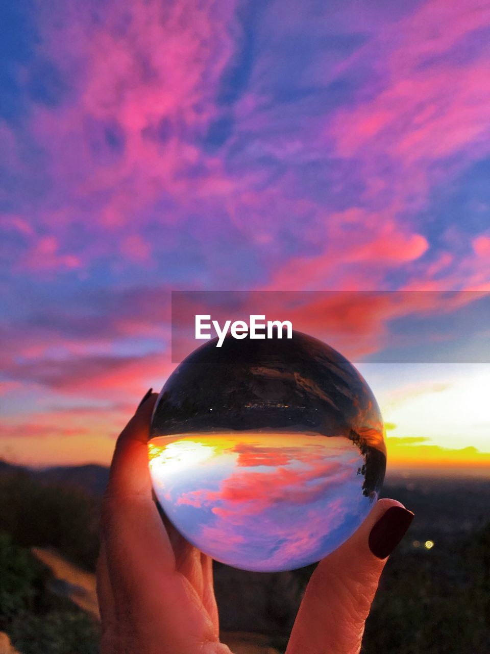 CROPPED IMAGE OF HAND HOLDING CRYSTAL BALL AGAINST SKY DURING SUNSET