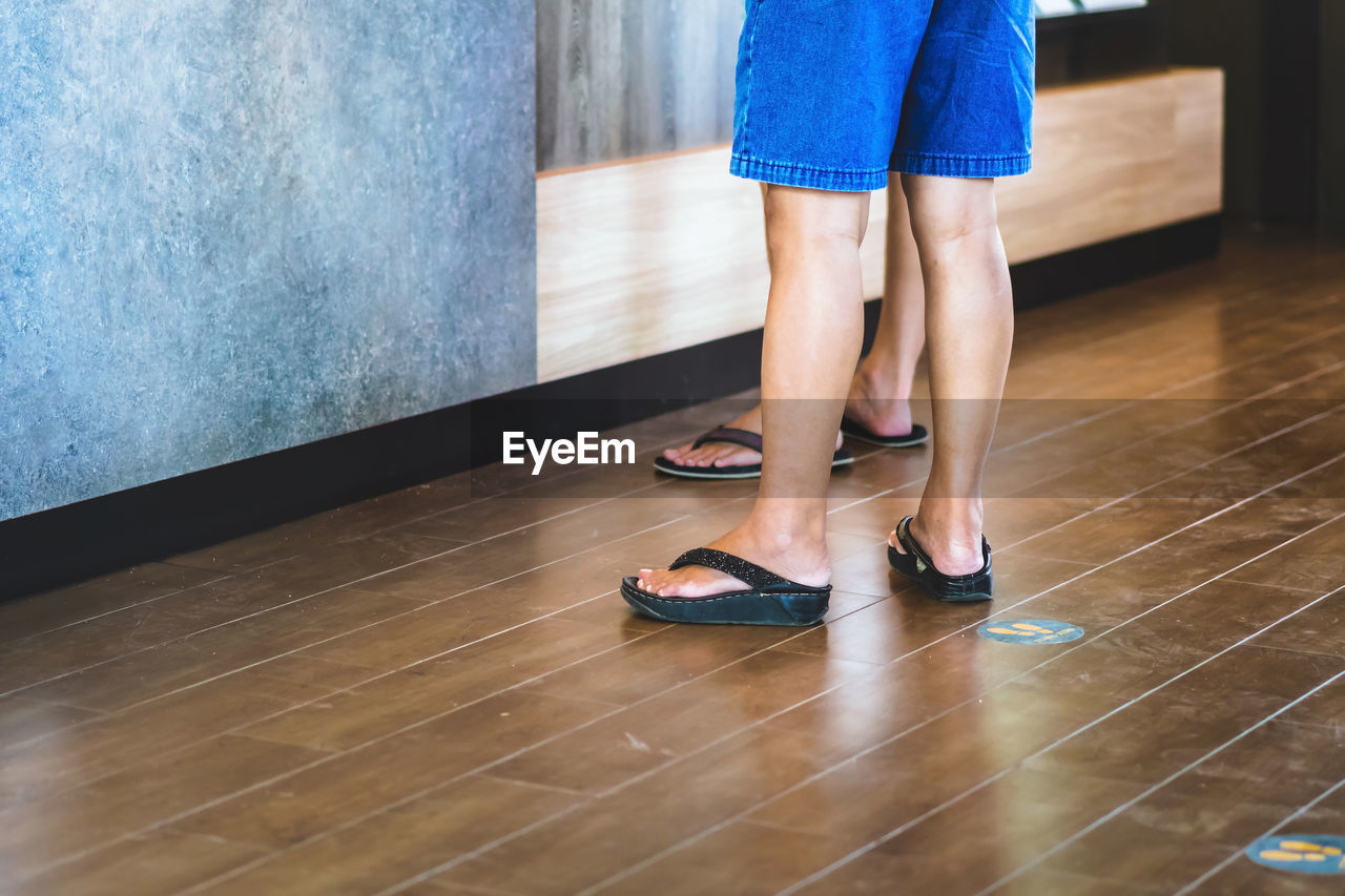 LOW SECTION OF WOMAN WEARING SHOES STANDING ON FLOOR