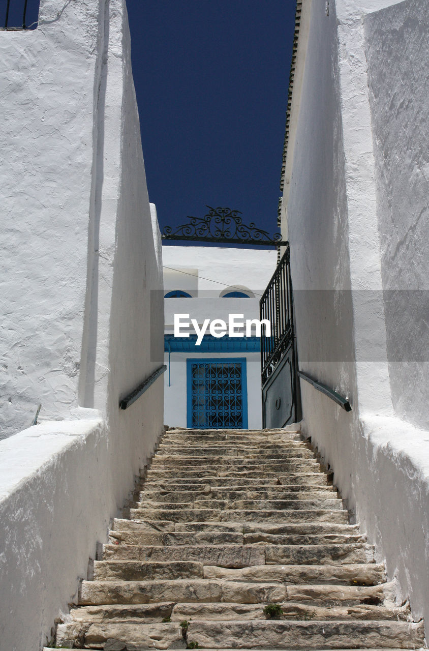 Low angle view of steps between white walls leading towards building to a clear blue sky