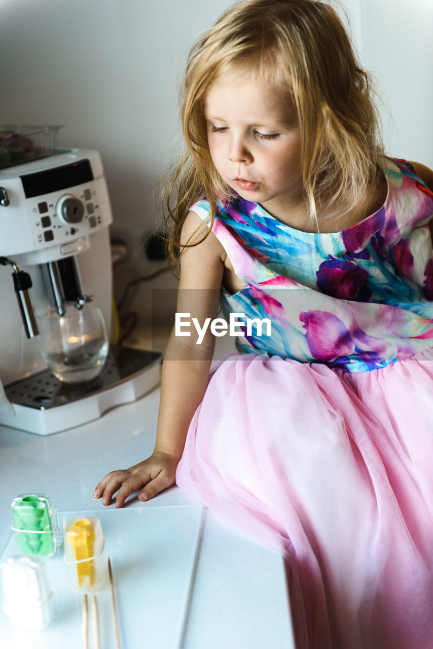 Little girl in elegant dress sitting on a table in the kitchen