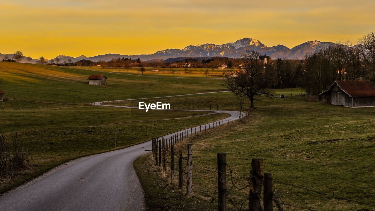 Road by agricultural field against sky during sunset