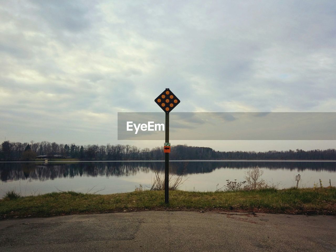 Sign board by calm lake against sky