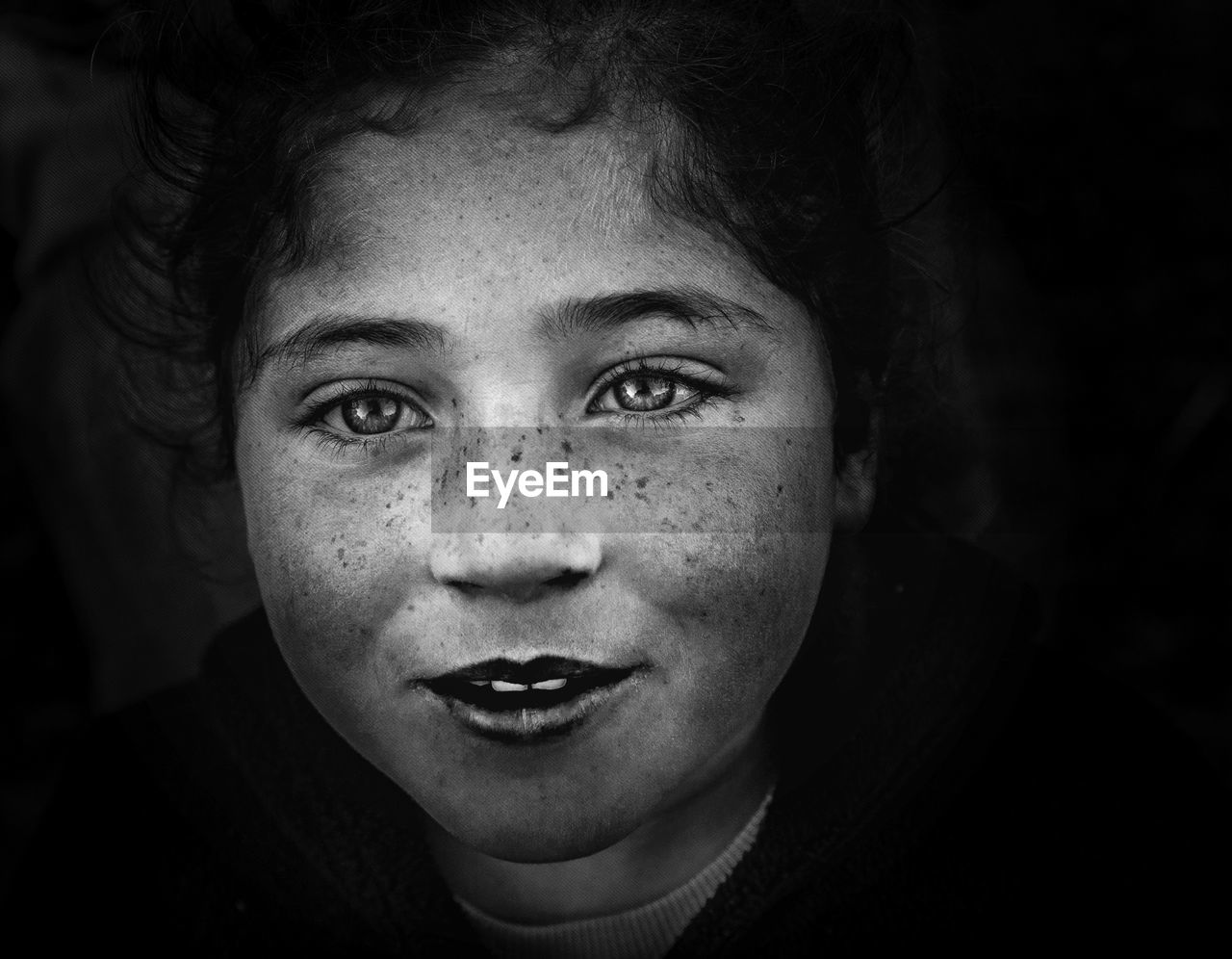 Close-up portrait of girl with freckles on face against black background