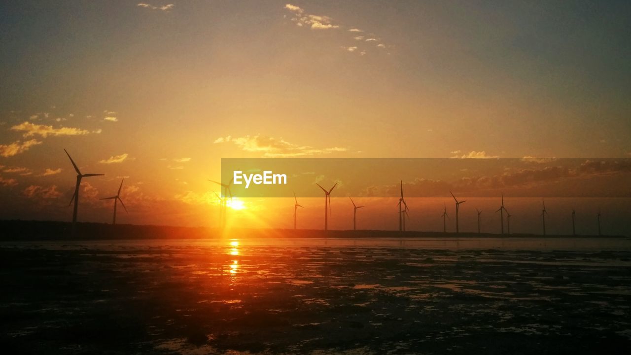 Wind turbines in distance with calm sea ahead at sunset