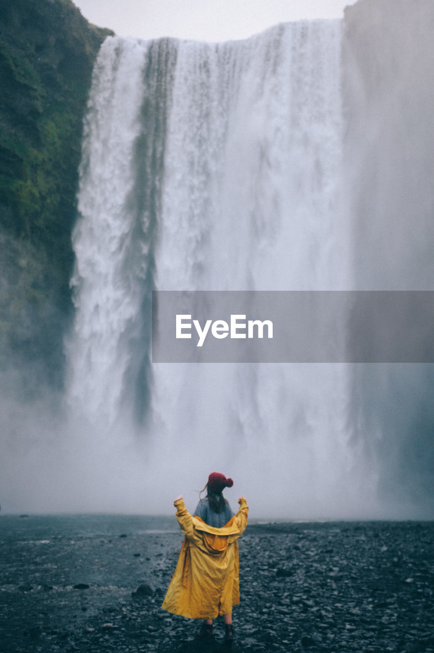 MAN STANDING IN SEA AGAINST WATERFALL