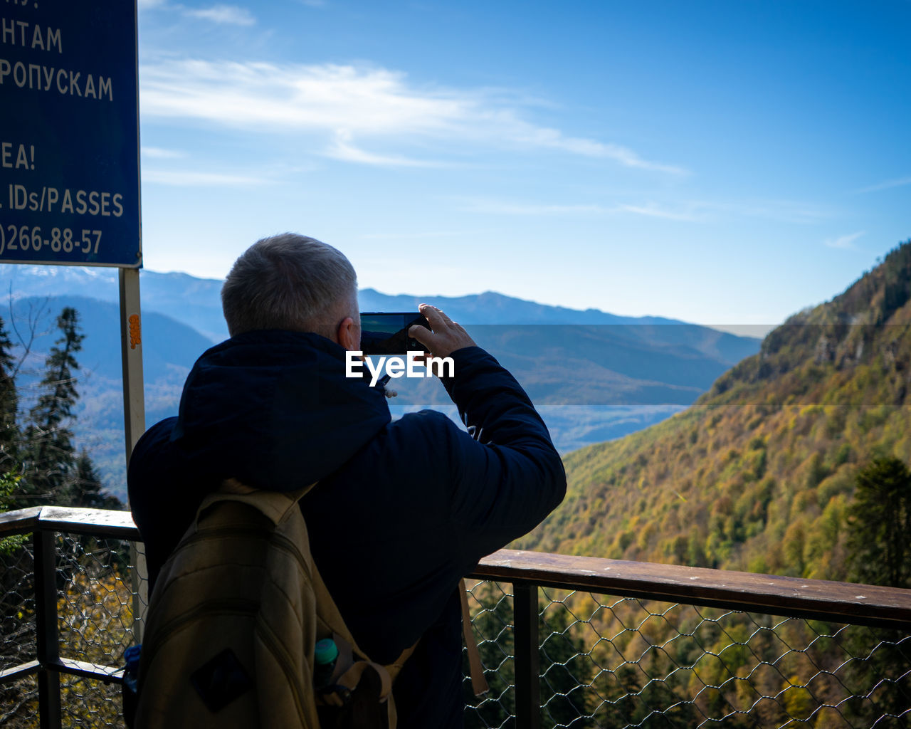 REAR VIEW OF MAN PHOTOGRAPHING AGAINST SKY