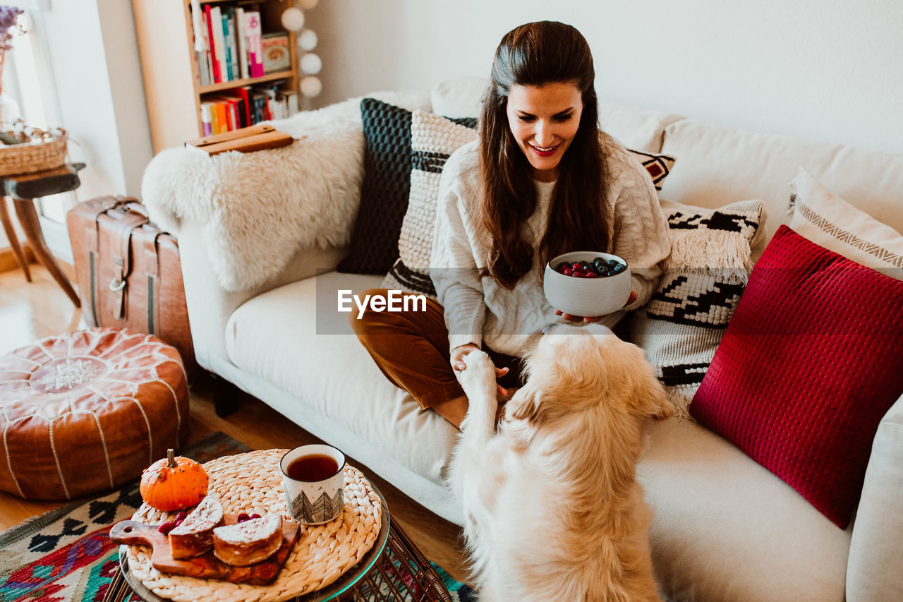 Woman holding food while playing with dog at home