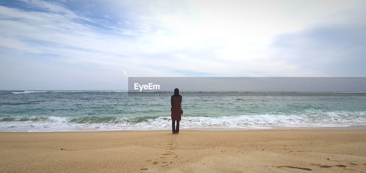 REAR VIEW OF PERSON STANDING ON BEACH