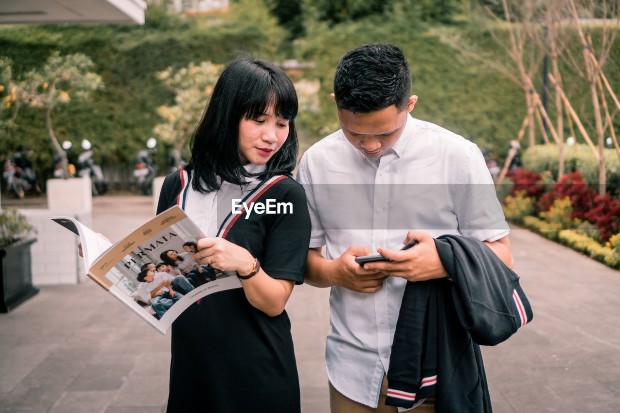 Man using mobile phone by woman on footpath