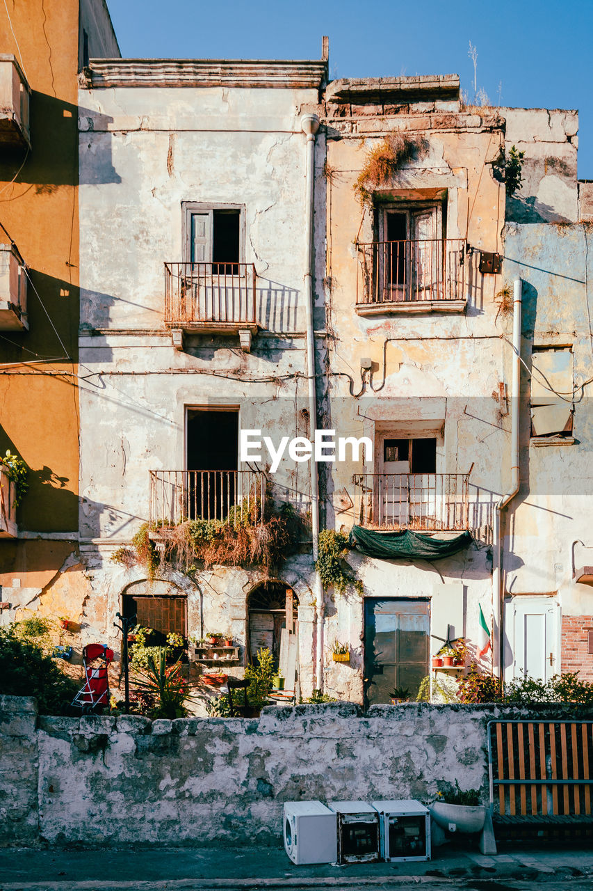 Ruined buildings in the old town of taranto with household waste on the street, vertical