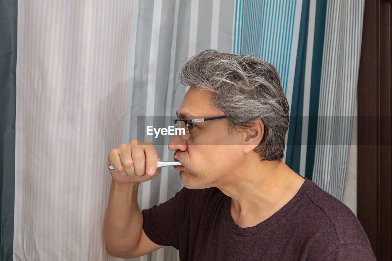 Adult gray-haired man brushes his teeth with a toothbrush in the bathroom