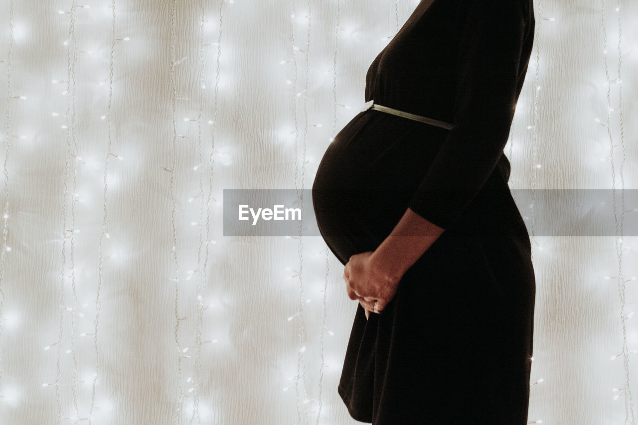 Midsection of pregnant woman standing against wall