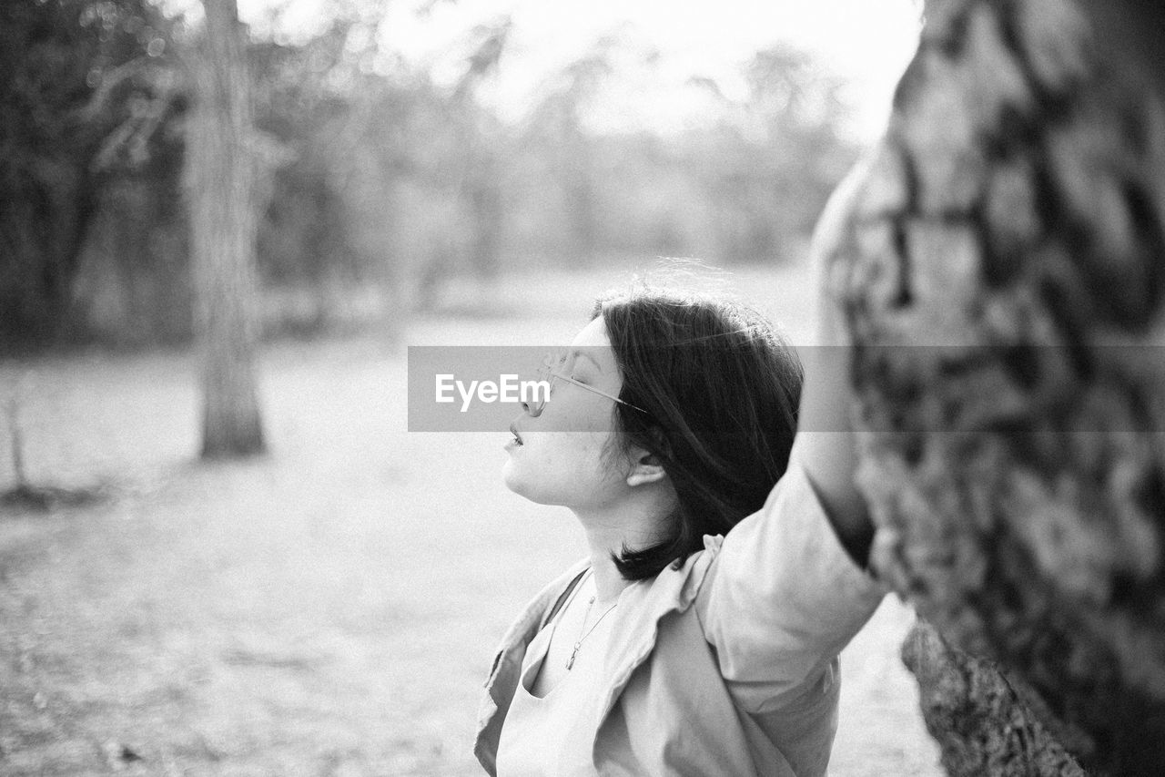 Close-up of woman with closed eyes standing by tree trunk