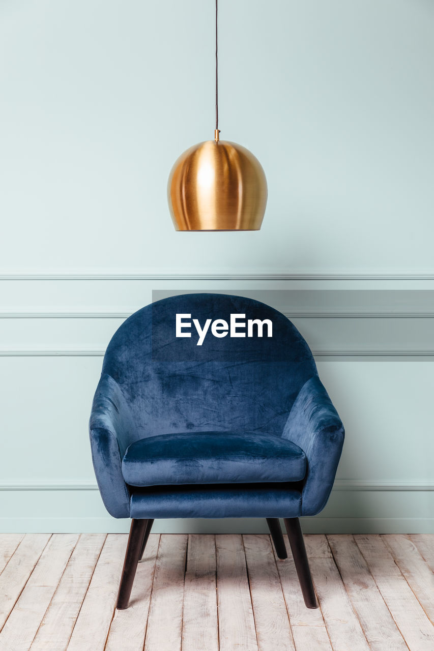 Blue armchair on turquoise background with a golden lamp