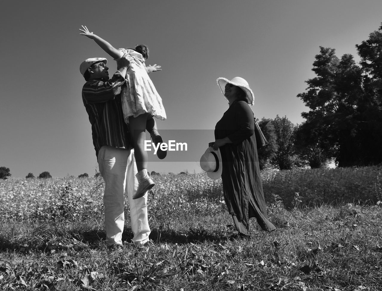 Father lifting her daughter while standing on field against sky