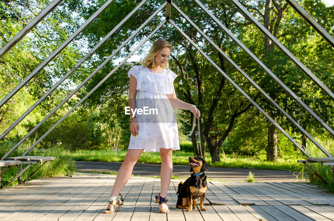 A beautiful blonde young woman with dog sitting next to her in the park.