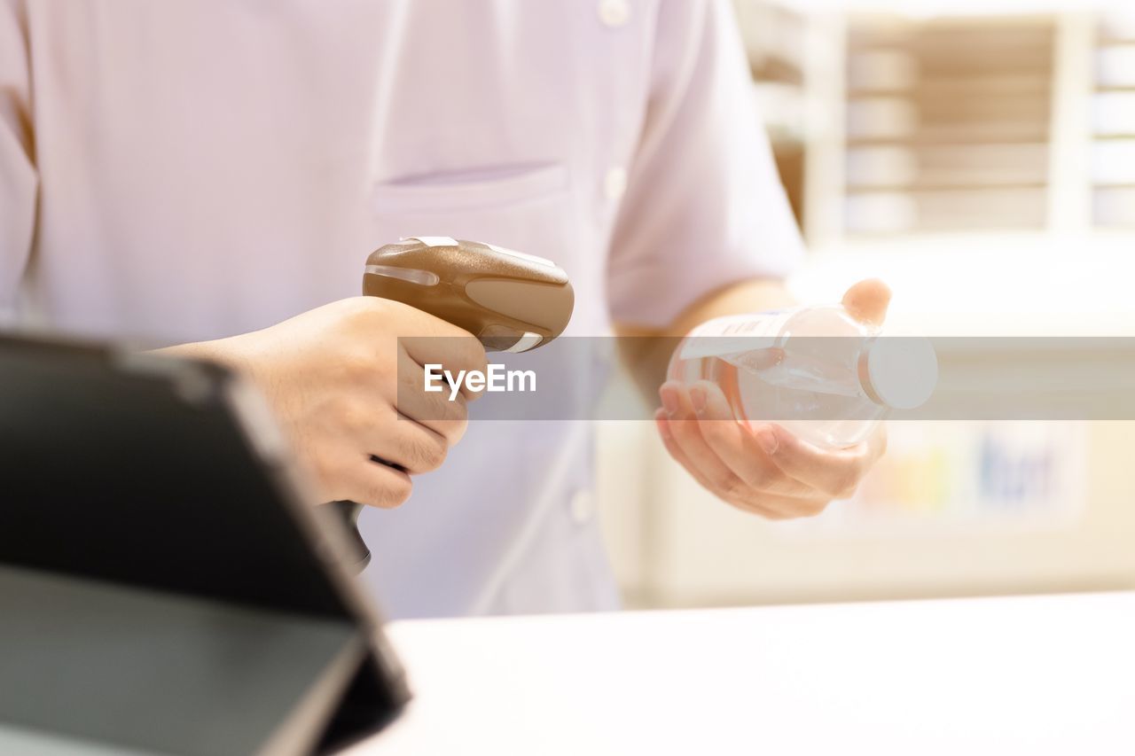 Midsection of man holding bar code reader and bottle by table in store