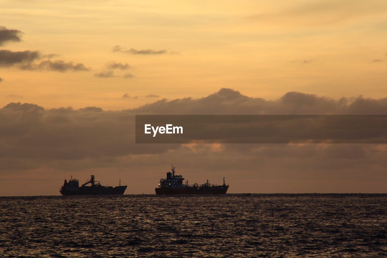 Ships on sea against cloudy sky during sunset