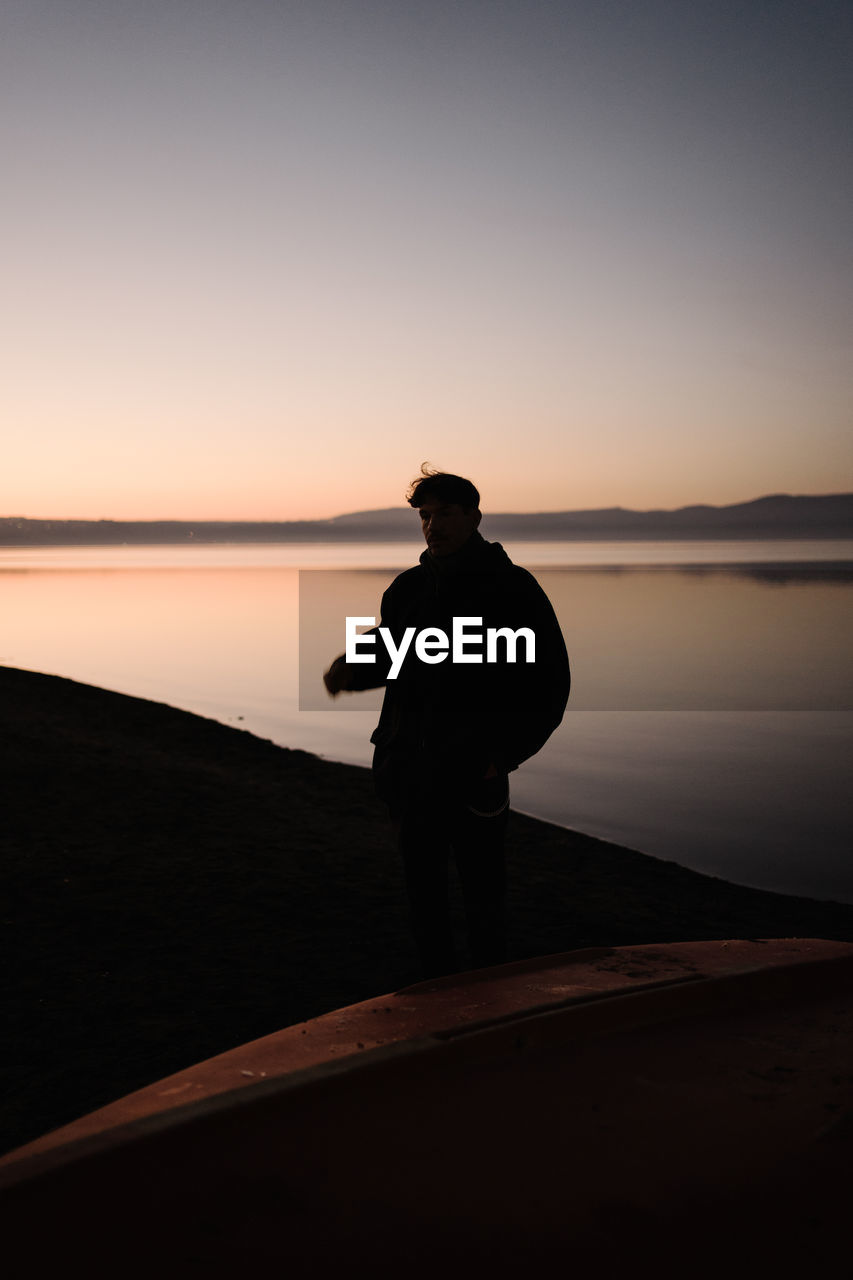 Silhouette man standing by lake against sky during sunset