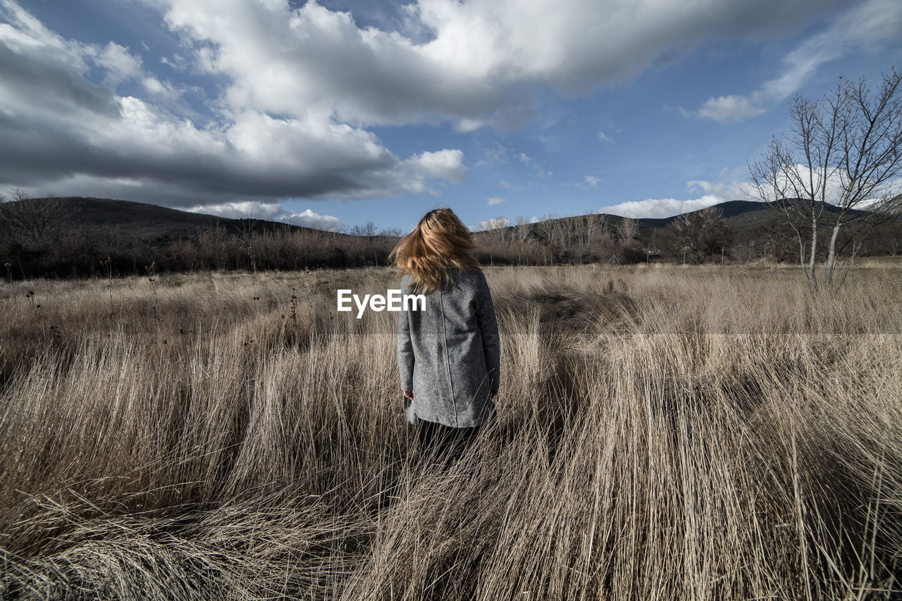 Rear view of woman standing on field against sky