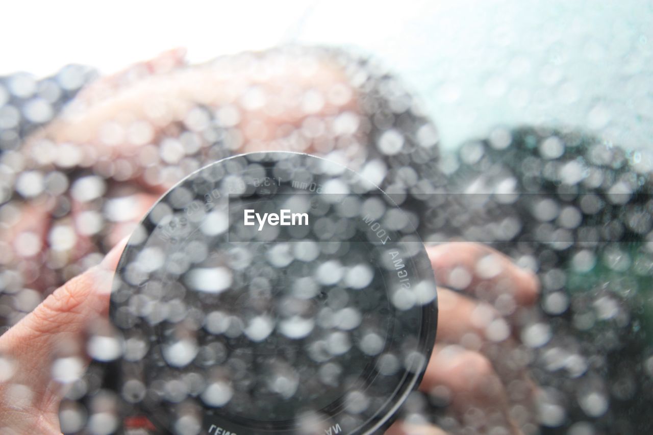 Close-up of person photographing with camera seen through wet car window