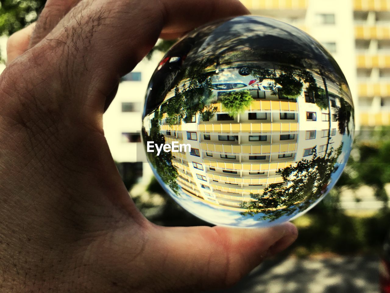 Cropped hand holding crystal ball against building