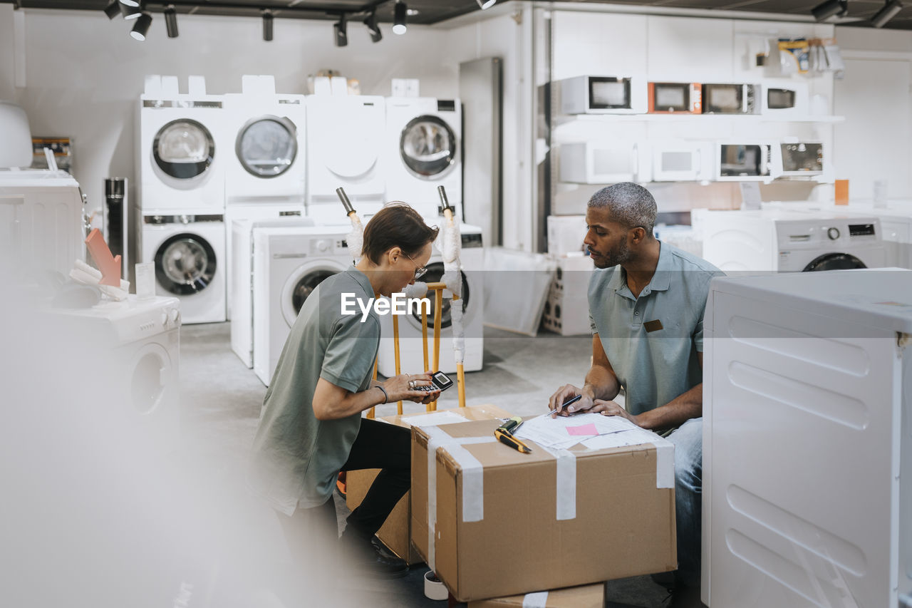 Multiracial male and female coworkers discussing over calculator while working in appliances store