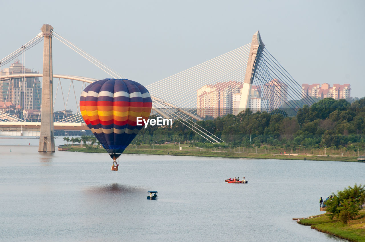 Hot air balloons over river against bridge