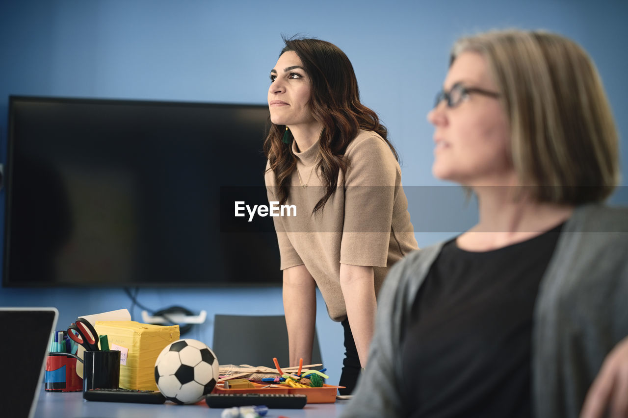 Mature female engineer looking away while standing by colleague at table in office