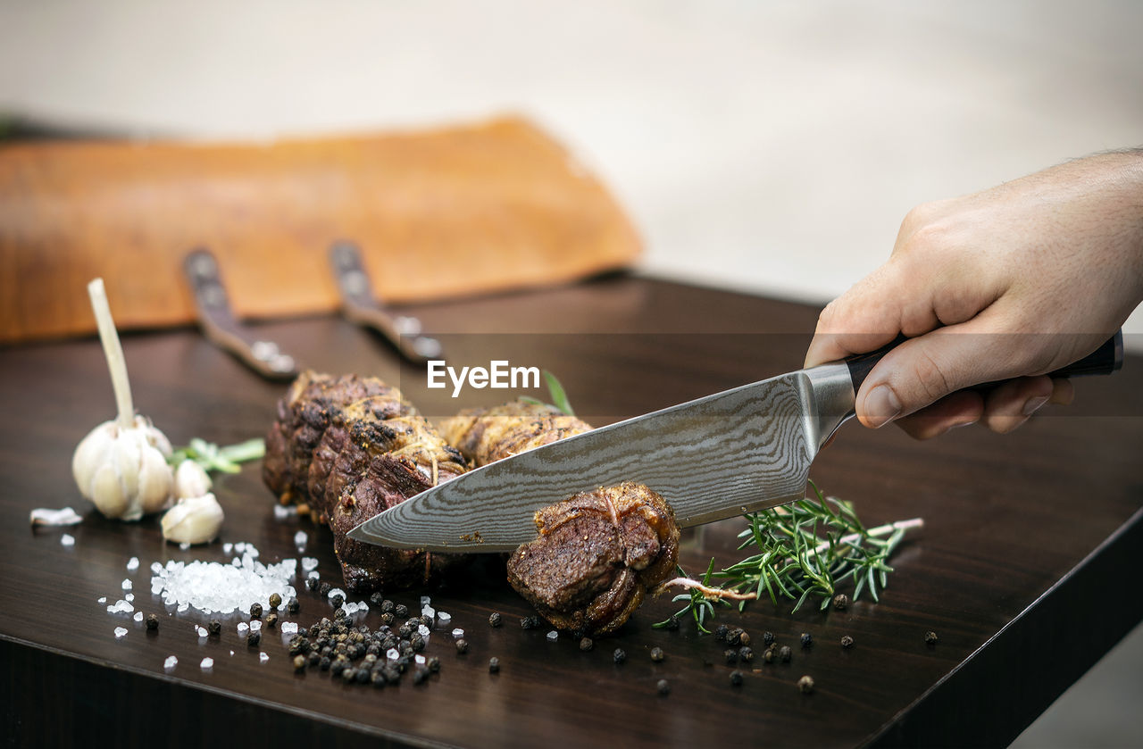 CLOSE-UP OF HAND HOLDING MEAT ON CUTTING BOARD