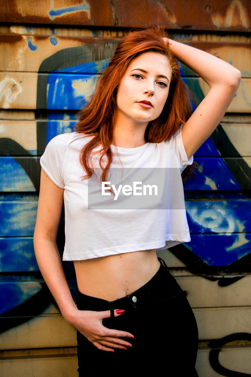 Portrait of beautiful young woman standing against graffiti wall