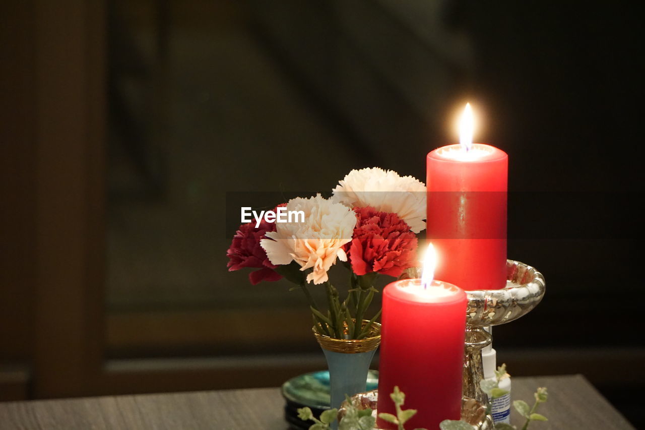 CLOSE-UP OF ILLUMINATED TEA LIGHT CANDLES ON TABLE IN VASE
