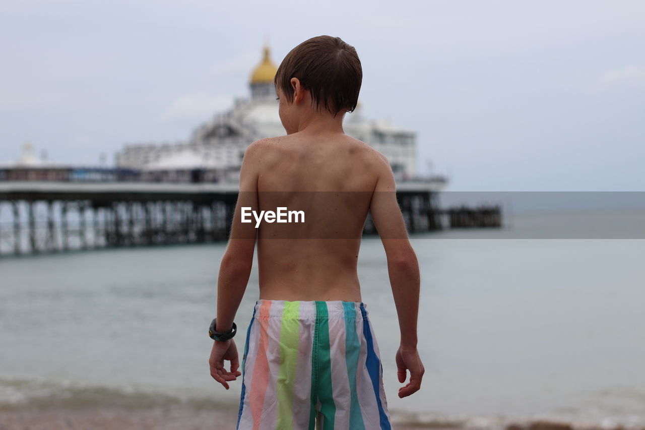 Rear view of shirtless boy looking at sea